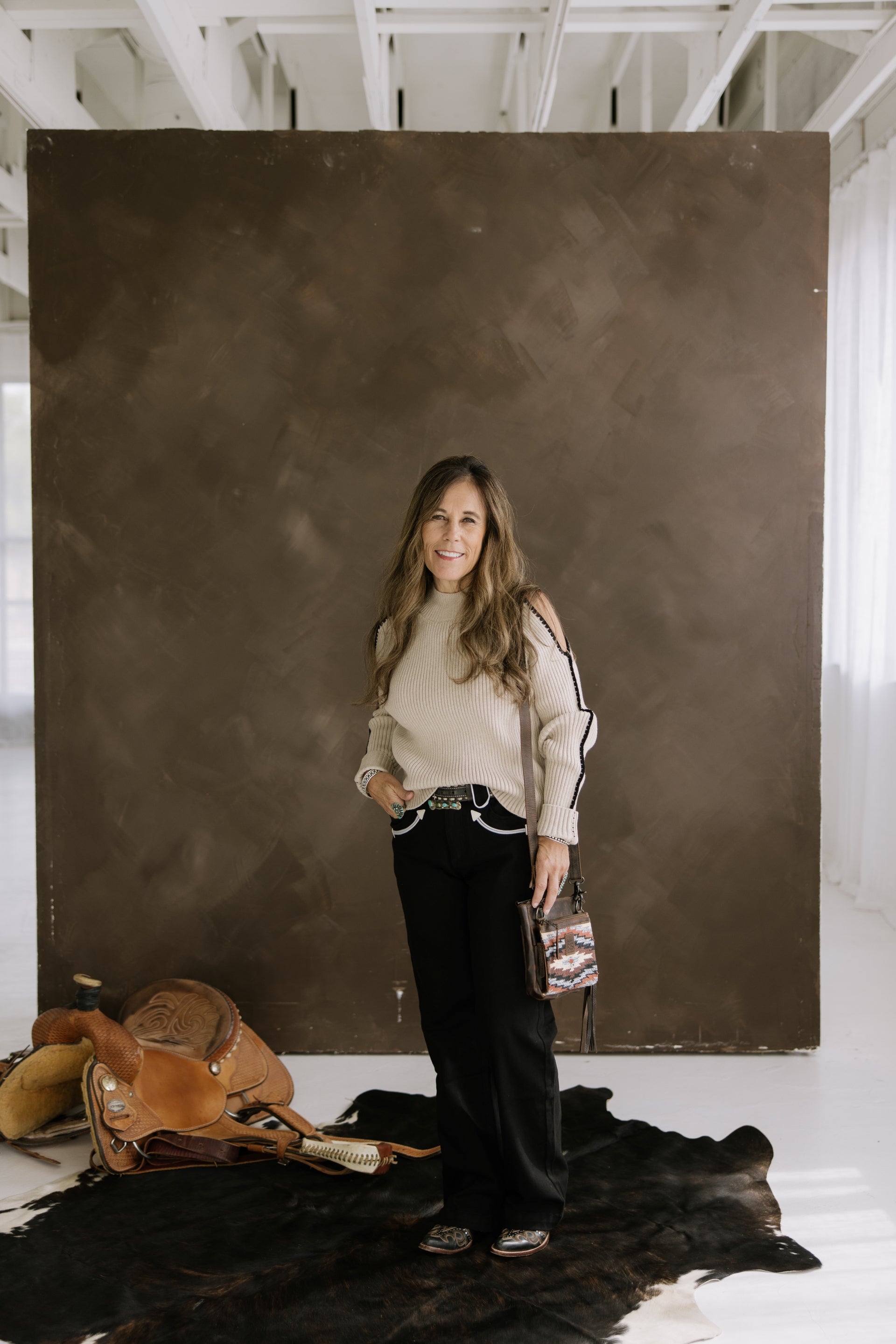 Woman standing in a room with a large brown leather bag and a black rug. Crooked Horn Co Western Fashion Boutique